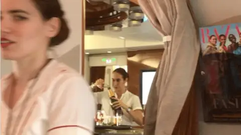 Una azafata rellena una copa de champán con los restos de otros pasajeros Una azafata rellena una copa de champán con los restos de otros pasajeros