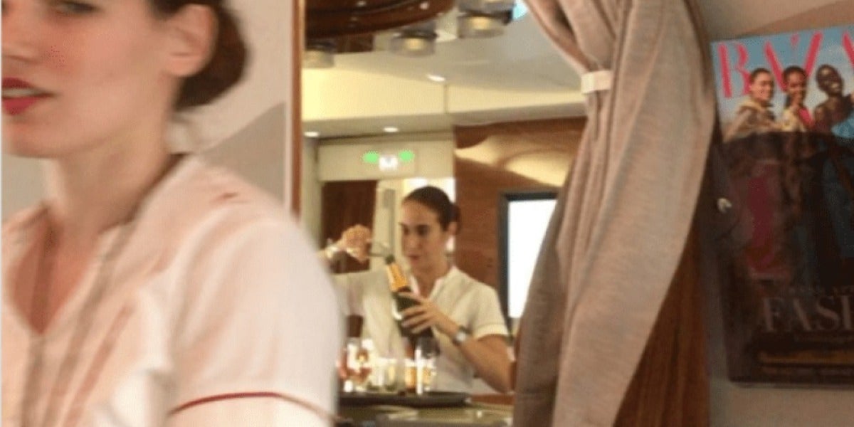 La azafata rellenando una botella de champagne con las sobras de la copas