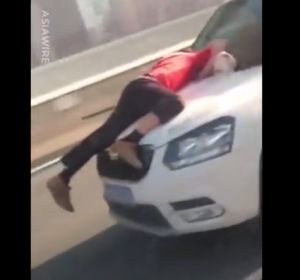 Un hombre aferrado al capó de un coche en marcha Un hombre aferrado al capó de un coche en marcha