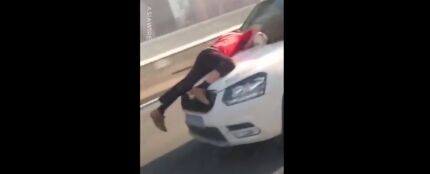 Un hombre aferrado al capó de un coche en marcha