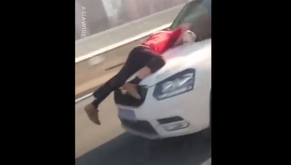 Un hombre aferrado al capó de un coche en marcha