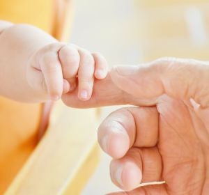 Una mano de adulto cogiendo la de un bebé Una mano de adulto cogiendo la de un bebé