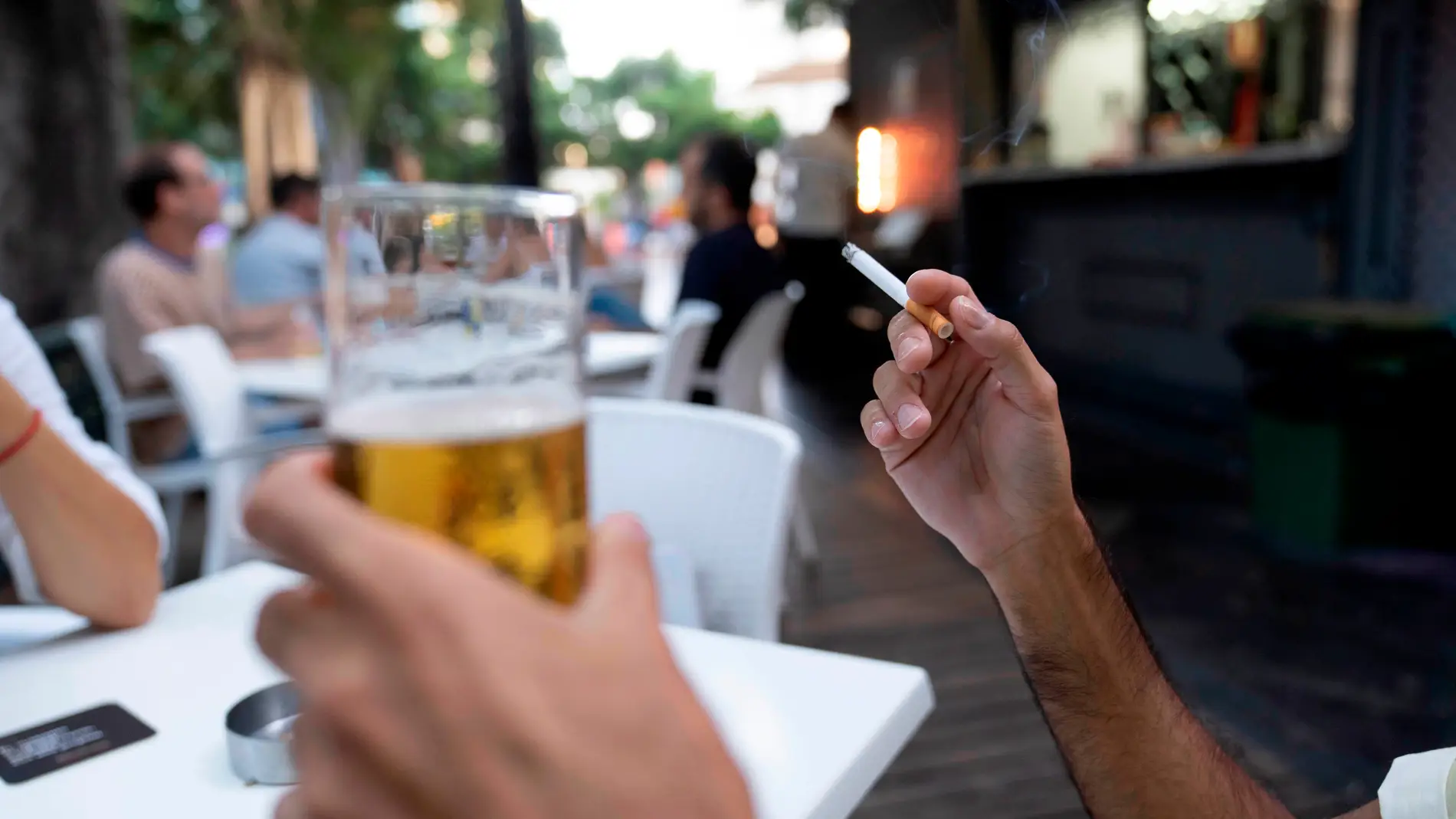 Una persona sostiene un cigarrillo en la terraza de en un bar title=