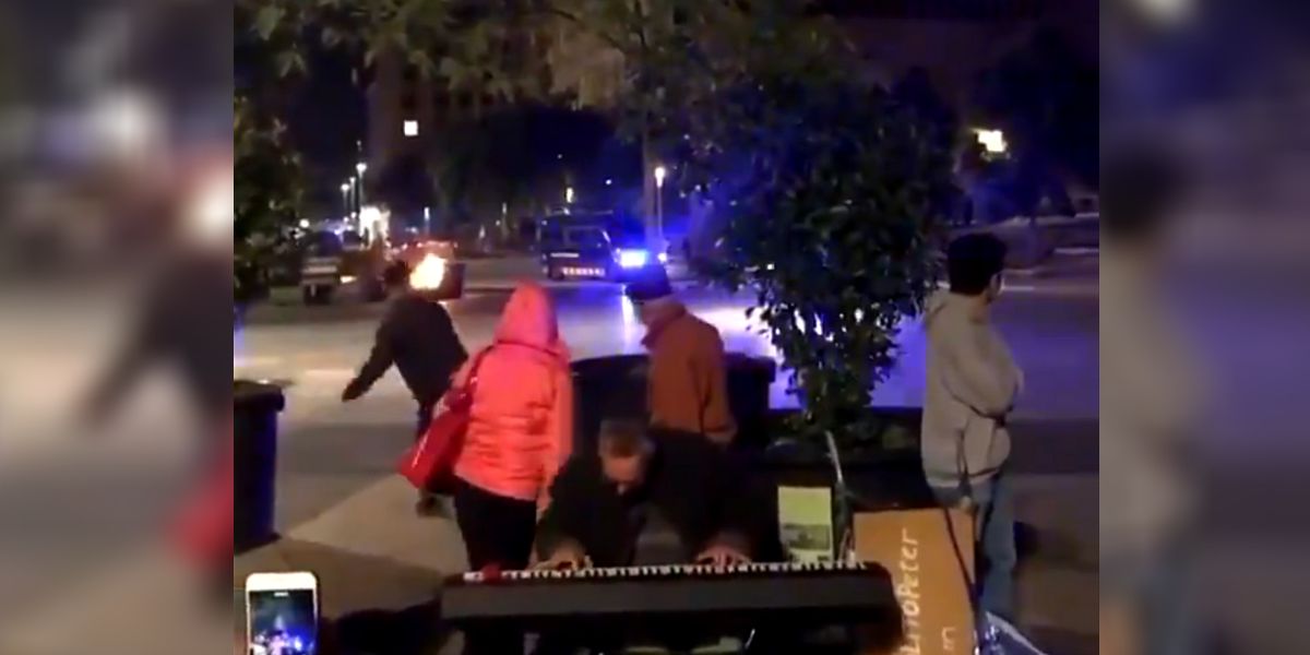 Un hombre toca con los disturbios de fondo en Barcelona