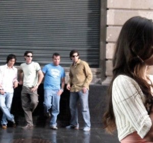 Un grupo de hombres observa a una mujer en la vía pública. Un grupo de hombres observa a una mujer en la vía pública.
