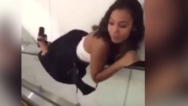 La chica bajando las escaleras mecánicas tumbada en el posamanos