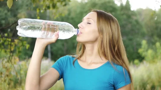 Una mujer bebiendo de una botella de plástico Una mujer bebiendo de una botella de plástico