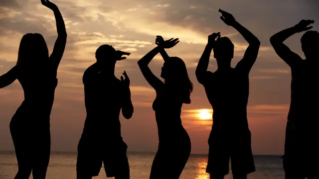 Siluetas de gente bailando en la playa