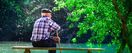 Fotografía de un hombre de avanzada edad, con bastón y boina, sentado en un banco frente a un estanque, en un parque. Fotografía de un hombre de avanzada edad, con bastón y boina, sentado en un banco frente a un estanque, en un parque.