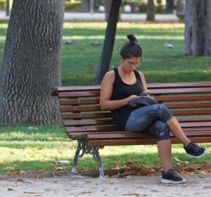 Imagen de archivo de una mujer que consulta su móvil en un banco del madrileño parque del Retiro Imagen de archivo de una mujer que consulta su móvil en un banco del madrileño parque del Retiro
