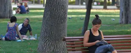 Imagen de archivo de una mujer que consulta su móvil en un banco del madrileño parque del Retiro Imagen de archivo de una mujer que consulta su móvil en un banco del madrileño parque del Retiro