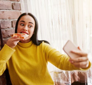 Chica grabándose en Instagram Stories mientras come una pizza Chica grabándose en Instagram Stories mientras come una pizza