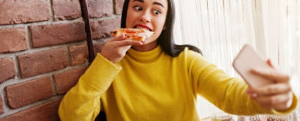 Chica grabándose en Instagram Stories mientras come una pizza