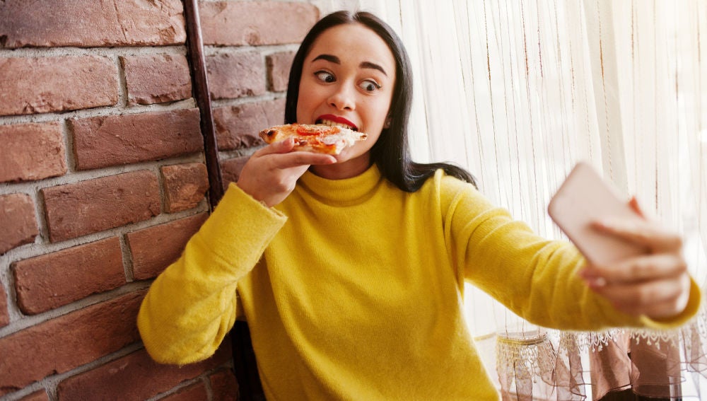 Chica grabándose en Instagram Stories mientras come una pizza