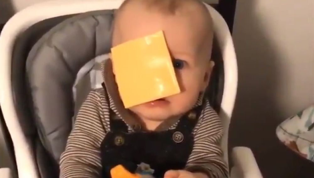 Un bebé con una loncha de queso en la cara.