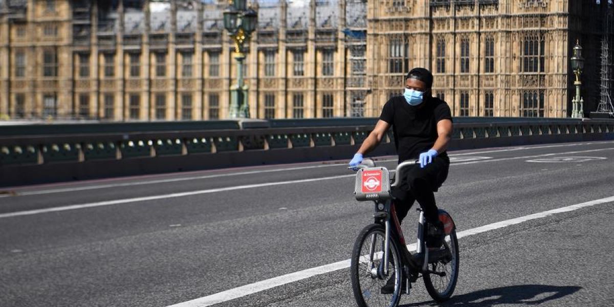 Un hombre con mascarilla circula en bicicleta frente al Parlamento británico en Londres