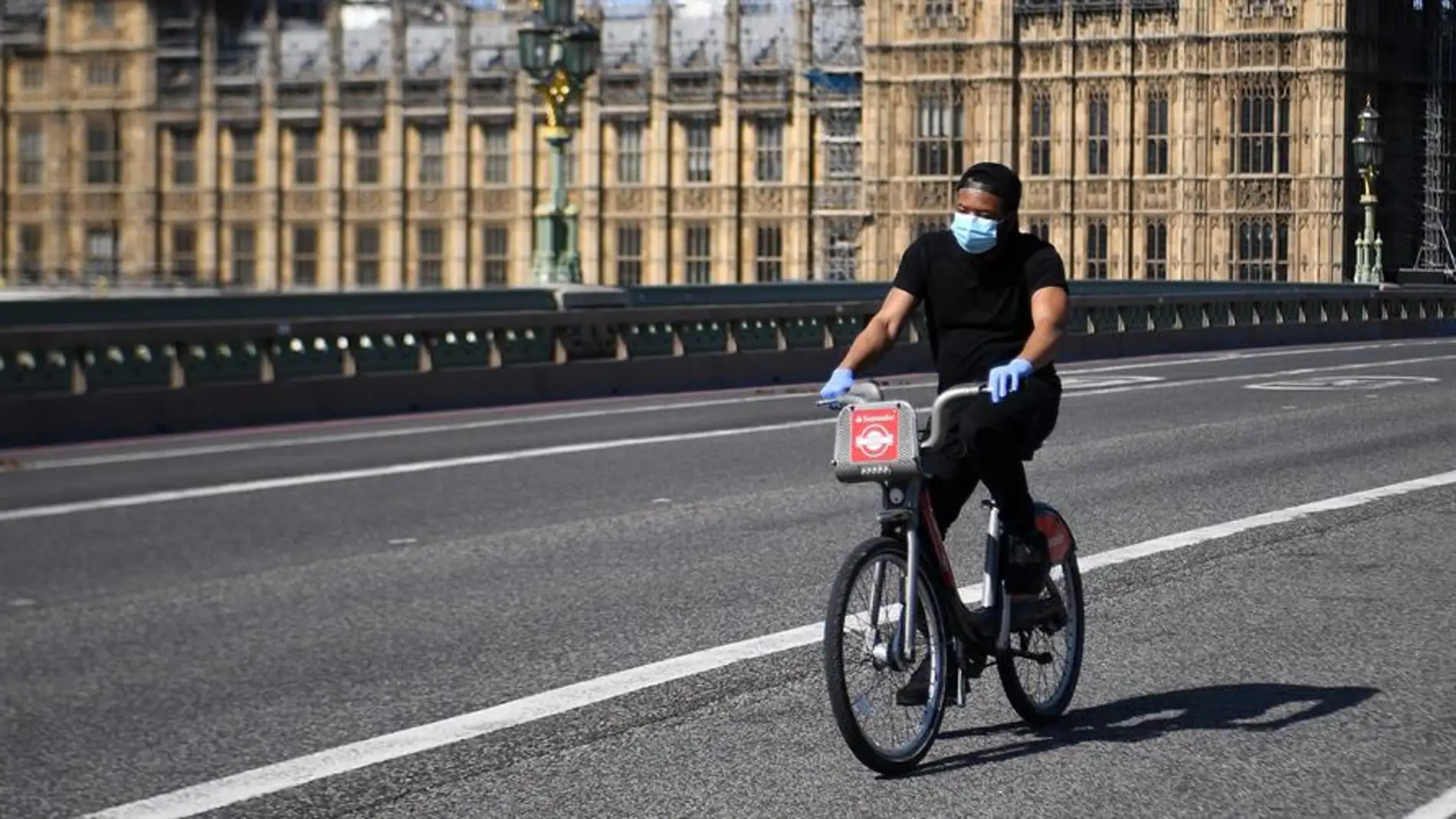 Un hombre con mascarilla circula en bicicleta frente al Parlamento británico en Londres title=