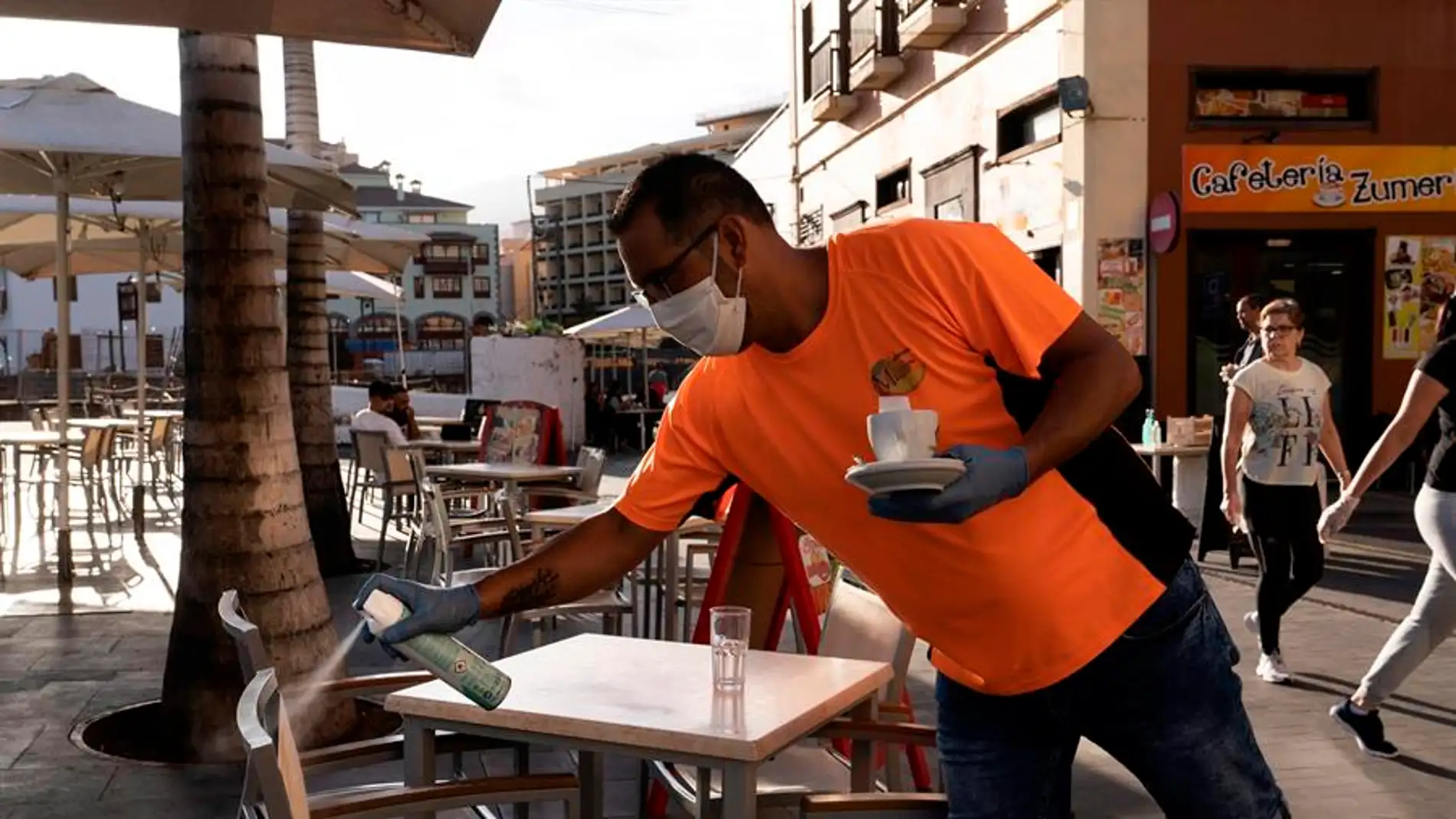 Un camarero desinfecta unas sillas de una terraza de un bar.