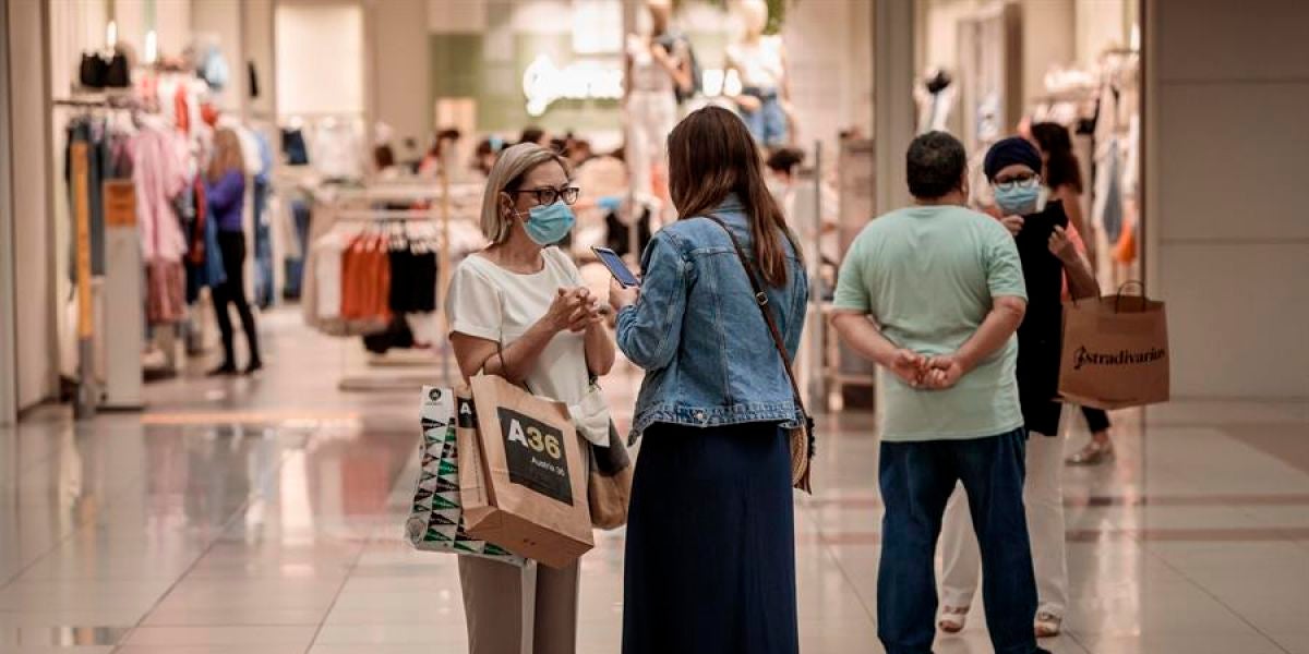 Varias personas realizan compras en un centro comercial con mascarillas.