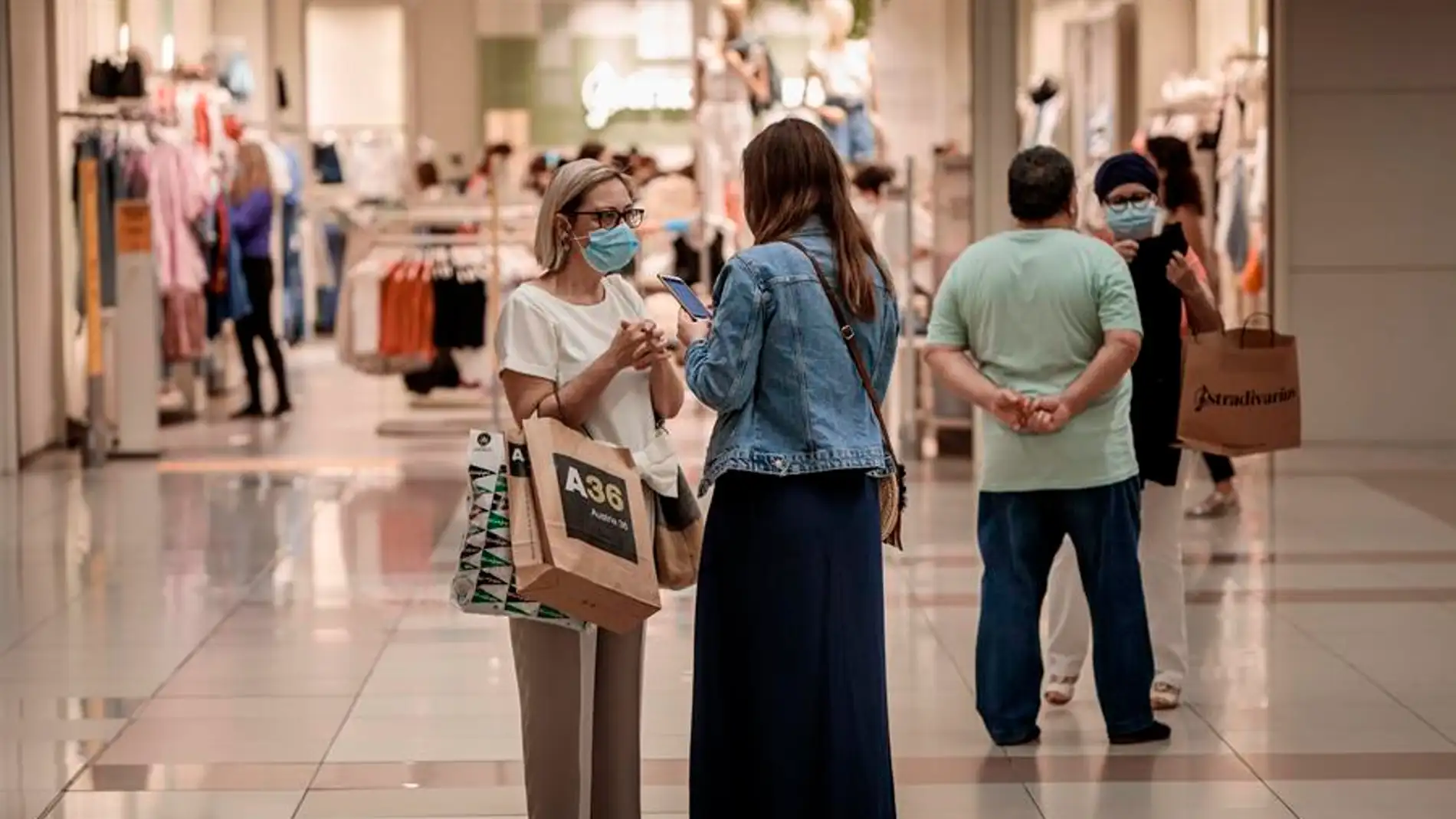 Varias personas realizan compras en un centro comercial con mascarillas. title=