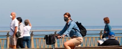 Una mujer pasea en bicicleta protegida con una mascarilla por el paseo de la Zurriola de San Sebasti&aacute;n