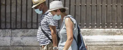 Dos personas caminan con mascarilla y sombrero Dos personas caminan con mascarilla y sombrero